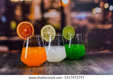 Tropical summer cocktails on a bar counter over restaurant lights background. Refreshing orange, white and green beverages. Copy space Royalty-Free Stock Photo #1417473797