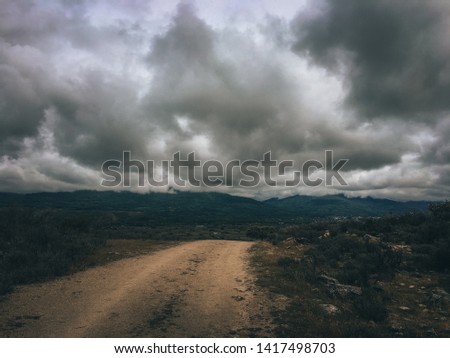 Path that leads to a landscape with huge mountains in a cloudy day