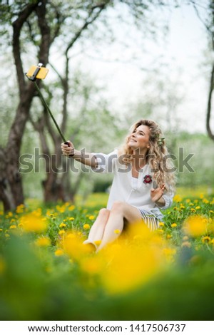
young beautiful blonde girl with beautiful hair sits in a field of dandelions and makes selfie