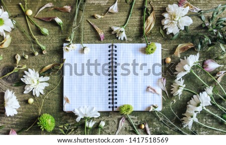 White notebook with white and green flowers on wooden table. Vintage old cards on green old background with wild flowers.