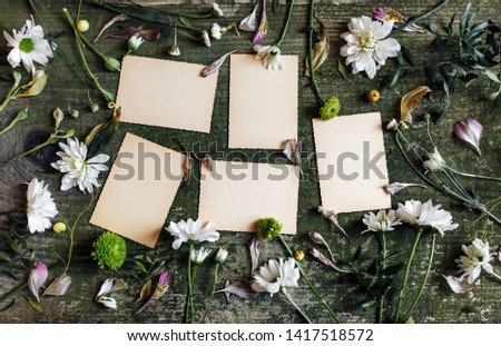 White sheets with white and green flowers on wooden table. Vintage old cards on green old background with wild flowers.