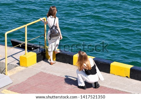 A girl takes a picture of her girlfriend on the edge of sea berth