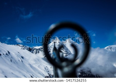 Looking trough a metal pointer at Snowy Mountain Peaks With Blue Sky Background, European Alps. 