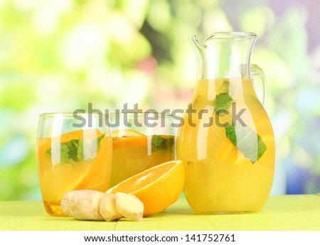 Orange lemonade in pitcher and glasses on wooden table on natural background
