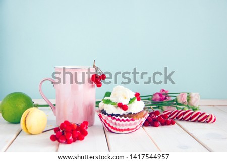 Pink tea mug with a handle next to a cream cake, lollipops, macarons, flowers, lively red berries, pink peony. The concept of a sweet and tasty breakfast, copy space