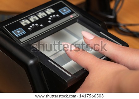 The process of scanning fingerprints during the check at border crossing. Female hand puts fingers to the fingerprint scanner. Biometric, identity verification and border control, immigration concept Royalty-Free Stock Photo #1417566503