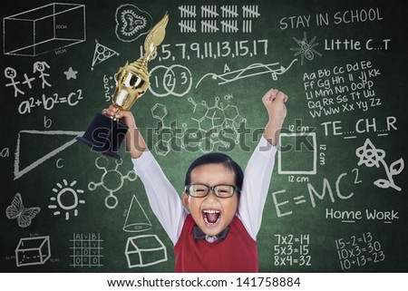 Happy student boy shouting while holding a trophy in classroom