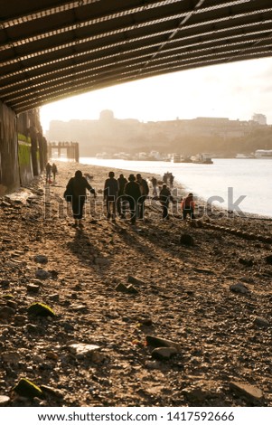 People are silhouetted against the light as they walk under the bridge when the river is at ebb tide