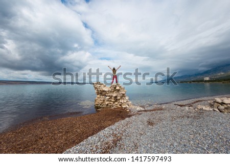 The girl stands on a pile of stones and looks at the sea. Woman resting on the sea coast. Tourist explores the sights of Croatia. Female silhouette against the sunset sky.