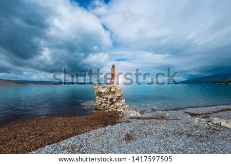 The girl stands on a pile of stones and looks at the sea. Woman resting on the sea coast. Tourist explores the sights of Croatia. Female silhouette against the sunset sky.