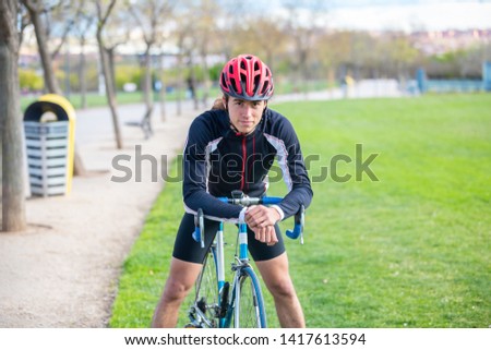 Smiling young fit male cyclist in sportswear and helmet sitting on bike in park and looking at camera