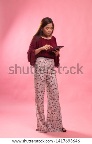 Full body of young Asian woman with a computer tablet on pink background