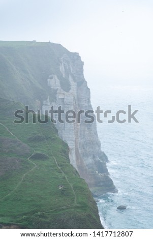 Portrait photo of steep cliffs going down to a rocky beach and the Atlantic ocean on a cloudy, foggy day. Shot in Etretat, Normandy, France. 