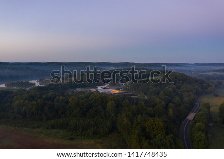 Aerial shot of foggy fields and forest near a highway