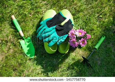 Close up of Gardening tools on the green grass lawn. Countryside view. Landscape. Still life. View of hoe, shovel, scoop, gloves and Rubber Shoes.