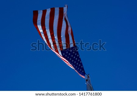 Looking up at American red, white, and blue flag on flagpole from directly below on windy day against clear blue sky.