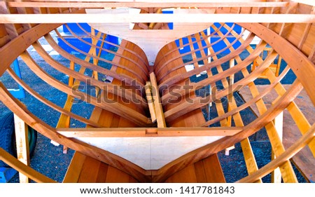 Small wooden boat in boatyard construction, timber structure with ribs, keel, bulkheads and longitudinal members in place.