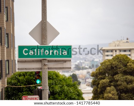 California street sign hanging in San Francisco in front of city and green light and a foggy sky