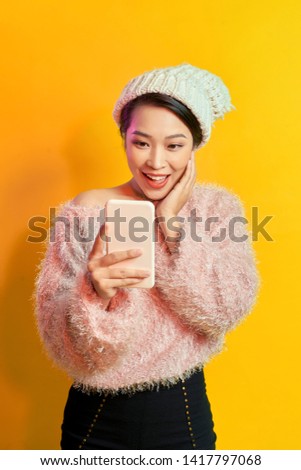 Excited short-haired woman holding smartphone on orange background. Indoor photo of wonderful female model with posing with phone.
