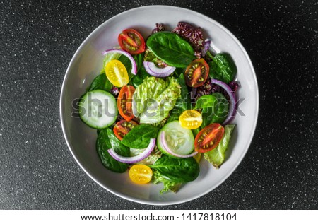 Top view of greens vegetable salad bowl with lettuce, spinach, cherry tomatoes, and red onion. Concept of healthy food, vegetarian and vegan food, fitness, sports, and lifestyle.