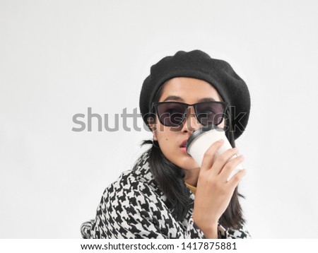Portrait of Asian woman wearing winter jacket and sitting on vintage brown bag, and drinking coffee cup.