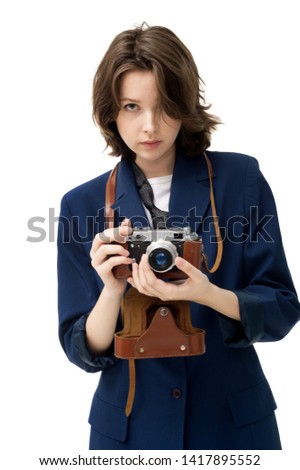 Beautiful brunette girl in a jacket and jeans on a white background posing with an old camera in a leather case, isolated