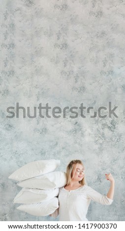 Professional housekeeping. Woman holding pile of pillows and showing biceps. Gray wall background. Copy space.