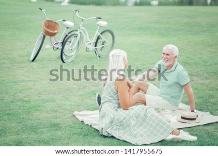 Happy birthday. Delighted aged man looking at his wife while giving a nice present to her for a birthday