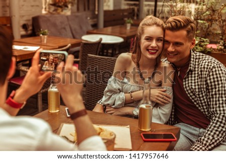 Happy couple. Happy loving beautiful nice-appealing young-adult smiling hugging radiant couple being photographed by their friend at the bar.