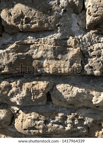 Natural textured rough cut blonde, grey and brown stone wall with cement mortar pointing using bricks and blocks casting shadows