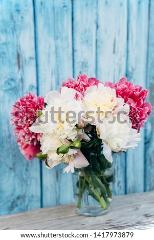 Bouquet of pink and white peonies in a vase on a blue wooden background