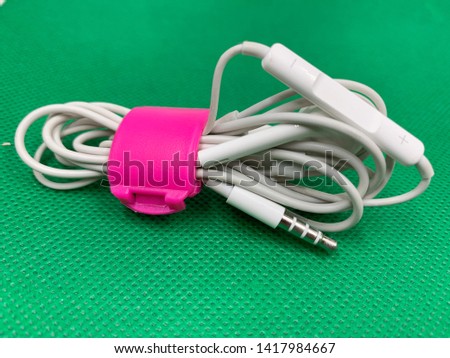 white earphone and cord is banded with pink plastic clip on green fabric Royalty-Free Stock Photo #1417984667