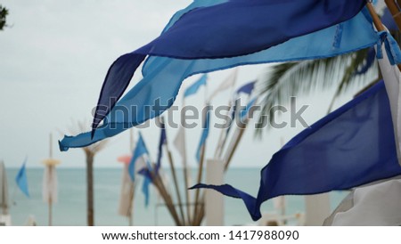 Blue flags waving in wind. Small triangular blue flags fluttering in wind in cloudy weather on tropical beach.