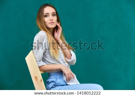 Picture a portrait of a beautiful girl woman with long dark flowing hair, fashionable, on a green background sitting on a wooden staircase. She sits in different poses and smiles. Made in studio