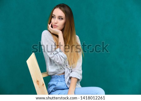 Picture a portrait of a beautiful girl woman with long dark flowing hair, fashionable, on a green background sitting on a wooden staircase. She sits in different poses and smiles. Made in studio