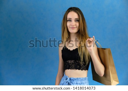 Photograph of a portrait of a beautiful girl woman with long dark flowing hair, loves shopping, on a blue background with packages. She is standing in different poses and smiling. Made in studio