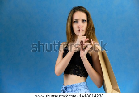Photograph of a portrait of a beautiful girl woman with long dark flowing hair, loves shopping, on a blue background with packages. She is standing in different poses and smiling. Made in studio