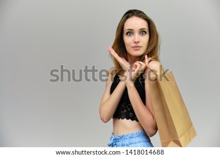 Photograph of a portrait of a beautiful girl woman with long dark flowing hair, loves shopping, on a gray background with packages. She is standing in different poses and smiling. Made in studio