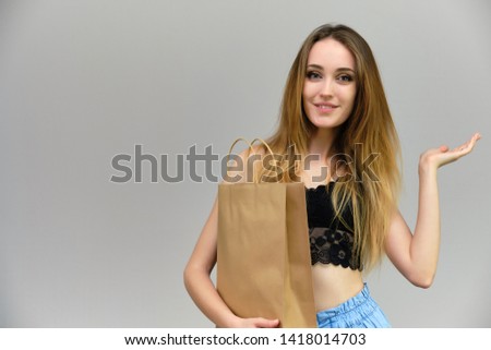 Photograph of a portrait of a beautiful girl woman with long dark flowing hair, loves shopping, on a gray background with packages. She is standing in different poses and smiling. Made in studio
