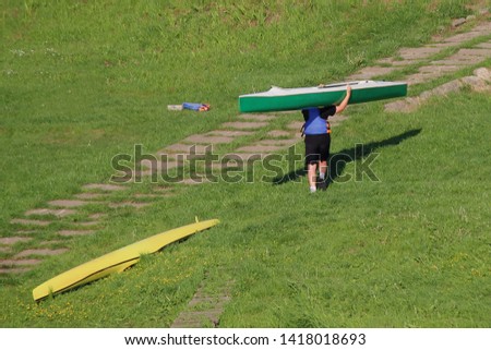 A boy kayaker carries a kayak on the shore - children's active vacation in sunny summer day