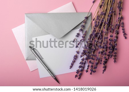 Blank paper in envelope and lavender flowers on pink background. Simple wedding arrangement. Top view