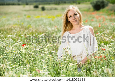 Beautiful young girl  in white dress  sitting in field of wild chamomile   flowers