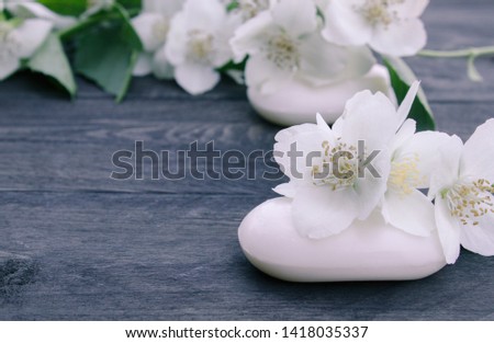 Cosmetic soap and white jasmine flowers with green leaves lie on a wooden background. There is a place for your text. Copy space