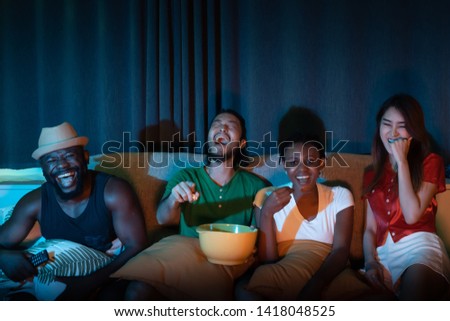 Group of friend sitting on sofa for watching television together, feeling fun and laughing emotional in the night light environment background at home