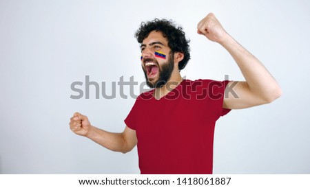 Sport fan screaming for the triumph of his team. Man with the flag of Venezuela makeup on his face and red t-shirt.