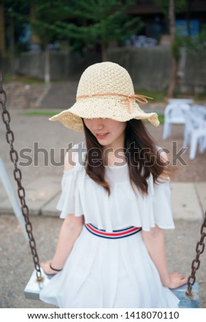 Schoolgirl wearing a white student skirt plays ukulele guitar while sitting on a swing