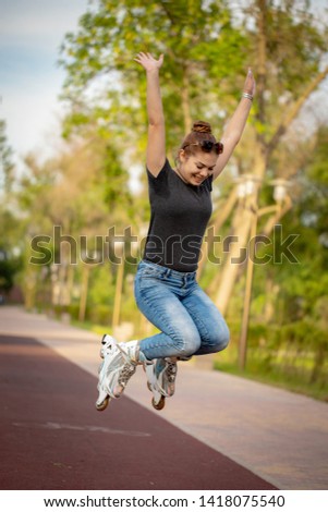 Beautiful, fitness young woman in black sportswear, to roller skate on the road. Cheerful woman on roller skates in the rays of the setting sun. Sports and fitness - concept of healthy lifestyle. 