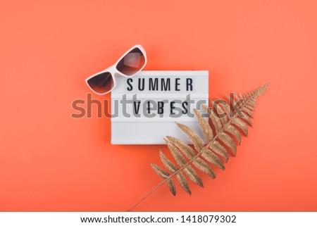 Summer vacations trip flat lay with Summer vibes text on light box, golden tropical leaves and Trendy white sunglasses. Colorful Hot Summer, vacations, travel concept. 
