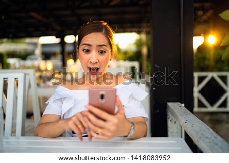 Mixed pretty smiling young woman holding and looking at smart phone on table white outdoor in sunset, enjoying summer vacation travel. in white derss