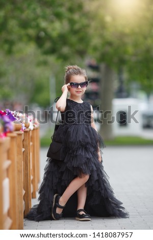 cute little girl in fashionable black dress on shopping. portrait of a kid with shopping bags. child in dress, sunglasses and shoes near cafe having fun. shopping. girl. fashion
